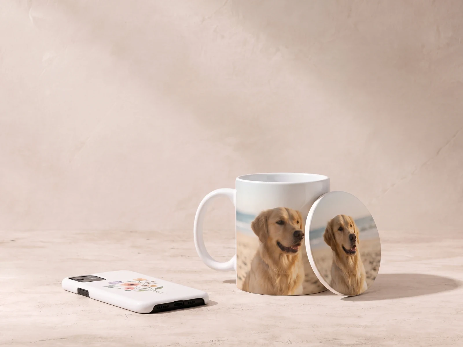 Weiße Tasse und Untersetzer mit Fotomotiv und eine Handyhülle mit Blumenmotiv vor heller Kalkputzwand